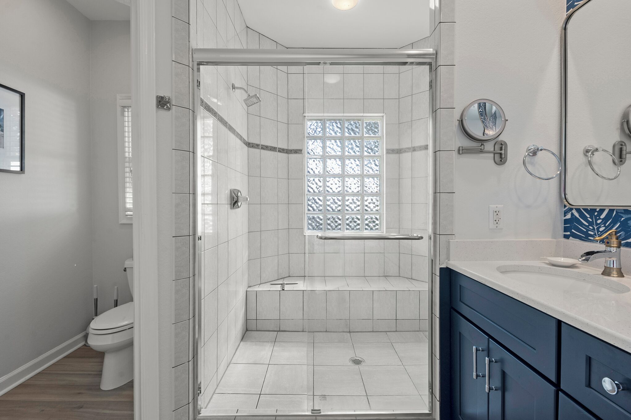 A modern bathroom with a glass-enclosed shower, a toilet, and a vanity with a sink and mirror.