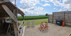 Relax on the patio with a round table, two chairs, and a grill, surrounded by a scenic green field.