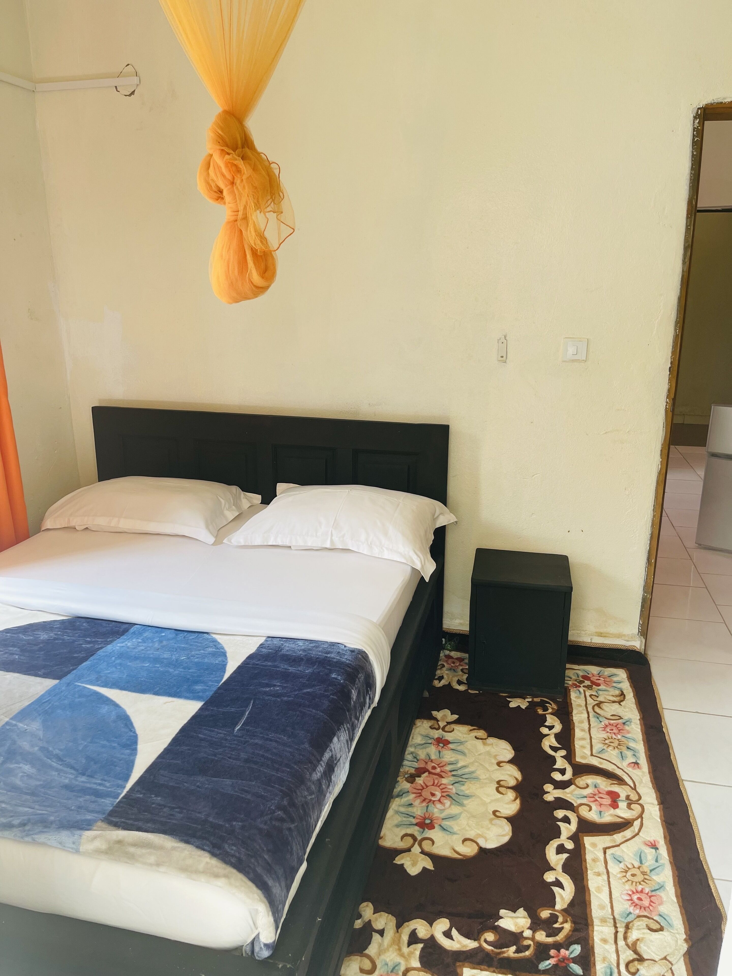 A bed with a black headboard, white pillows, and a blue and white blanket. There is a small black nightstand beside the bed.