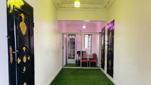A hallway with a green carpet, black doors with gold accents, and a person working at a desk in the background. - Hotel Svet Residence (Kribi)