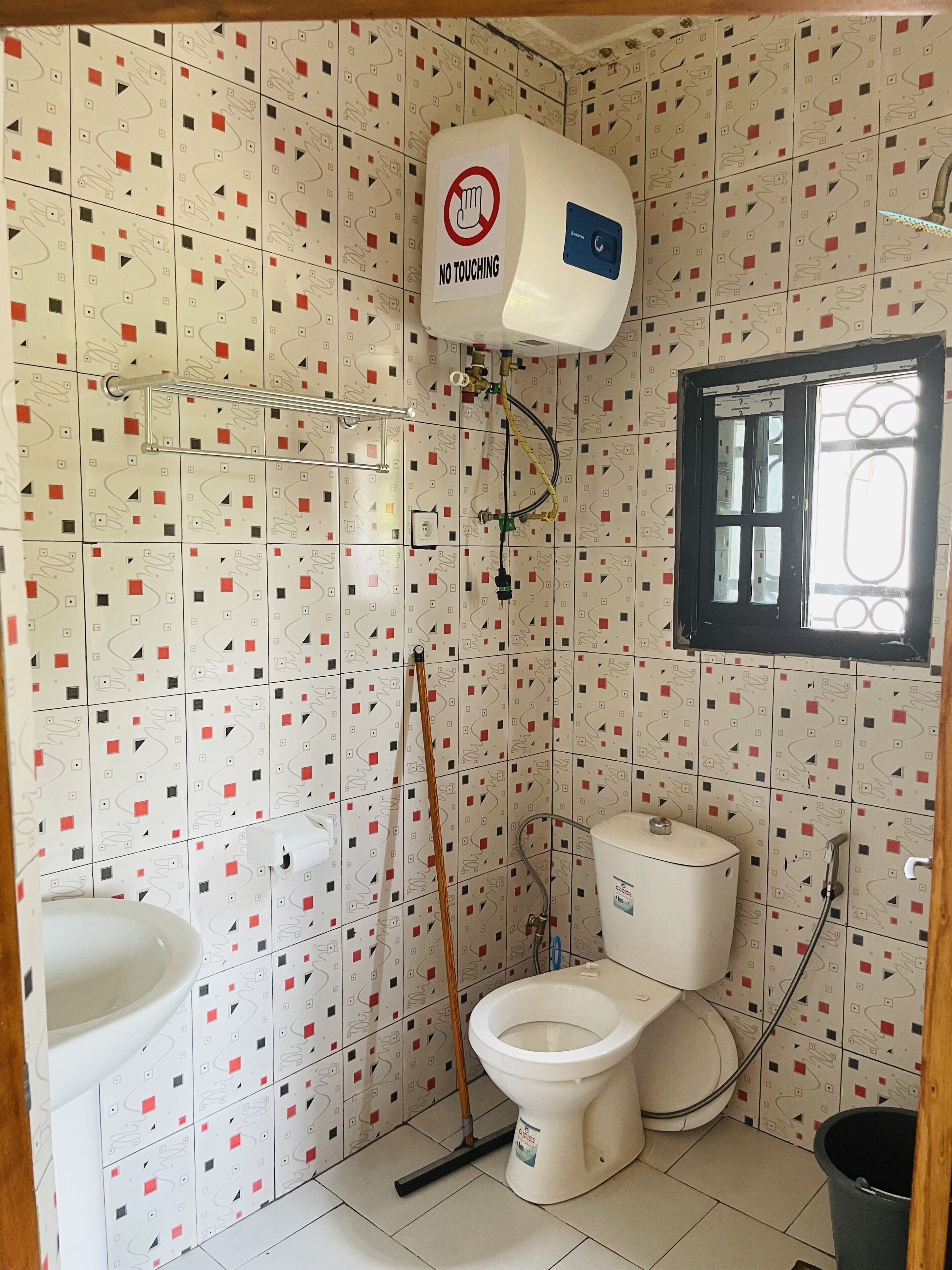 Baño con inodoro, bidé y lavamanos. Hay un cartel que dice 'No Touching' en la pared.