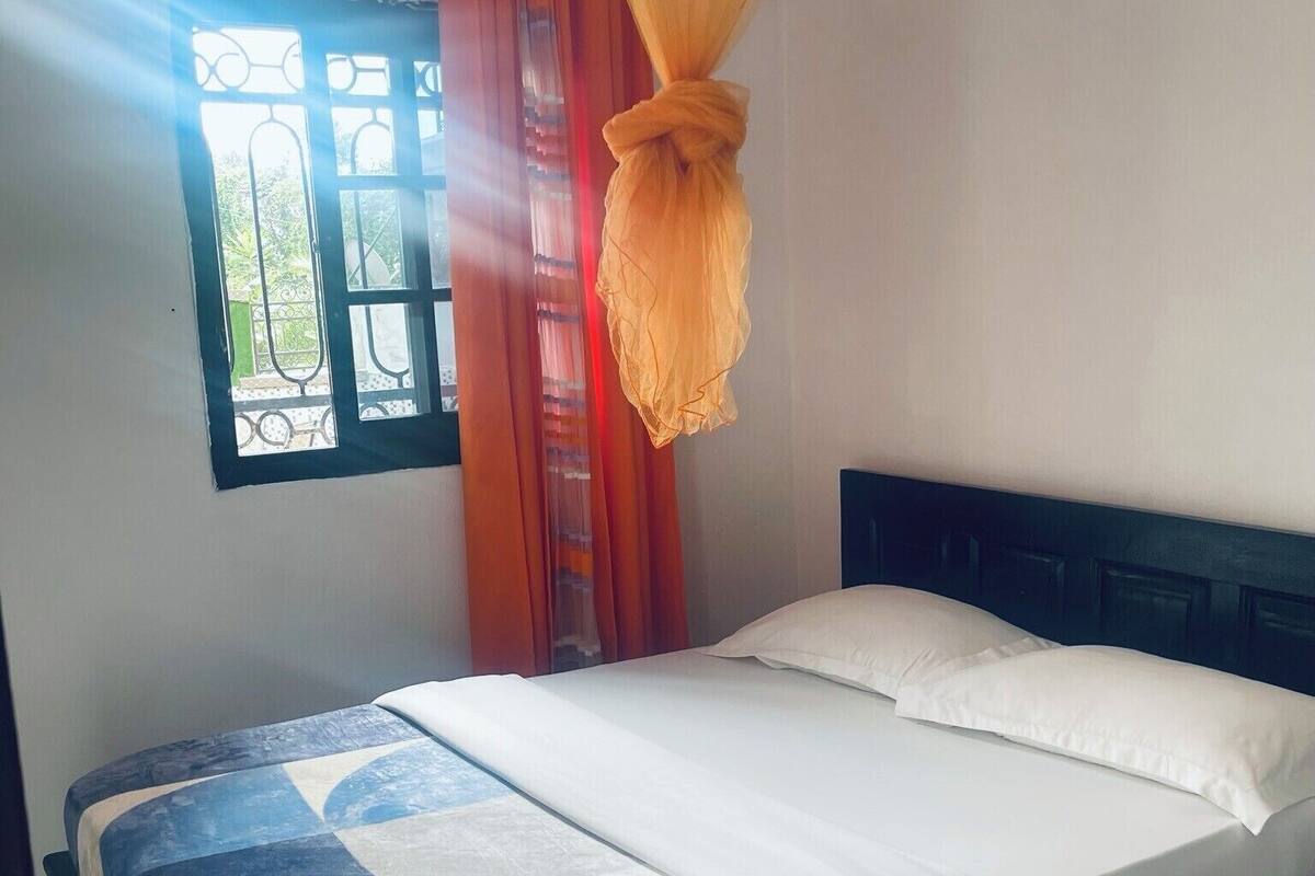 A bed with a blue and white quilt, white pillows, and an orange canopy.