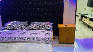 A bedroom with a zebra-patterned bedspread, a tufted headboard, a wooden nightstand, and a television on a cabinet. - Hotel Svet Residence (Kribi)