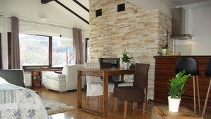 Ein gemütliches Wohnzimmer mit Steinwand, Kamin, Essbereich und großem Fenster.