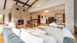 Ein geräumiges Wohnzimmer mit Kamin aus Stein, einer bequemen Couch, einem Essbereich und einem Fernseher.