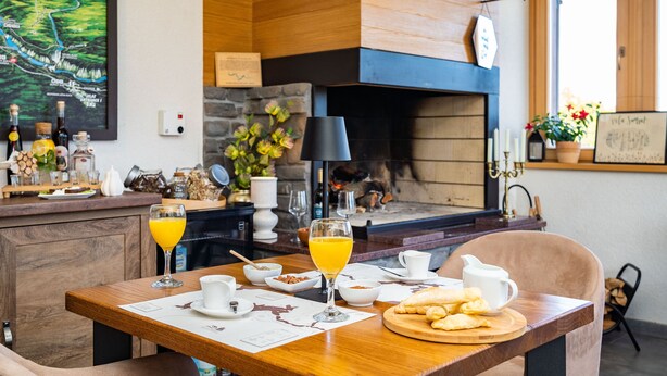 Ein Essbereich mit Holztisch, gedeckt für das Frühstück, einem Kamin und einem landschaftlichen Gemälde an der Wand.