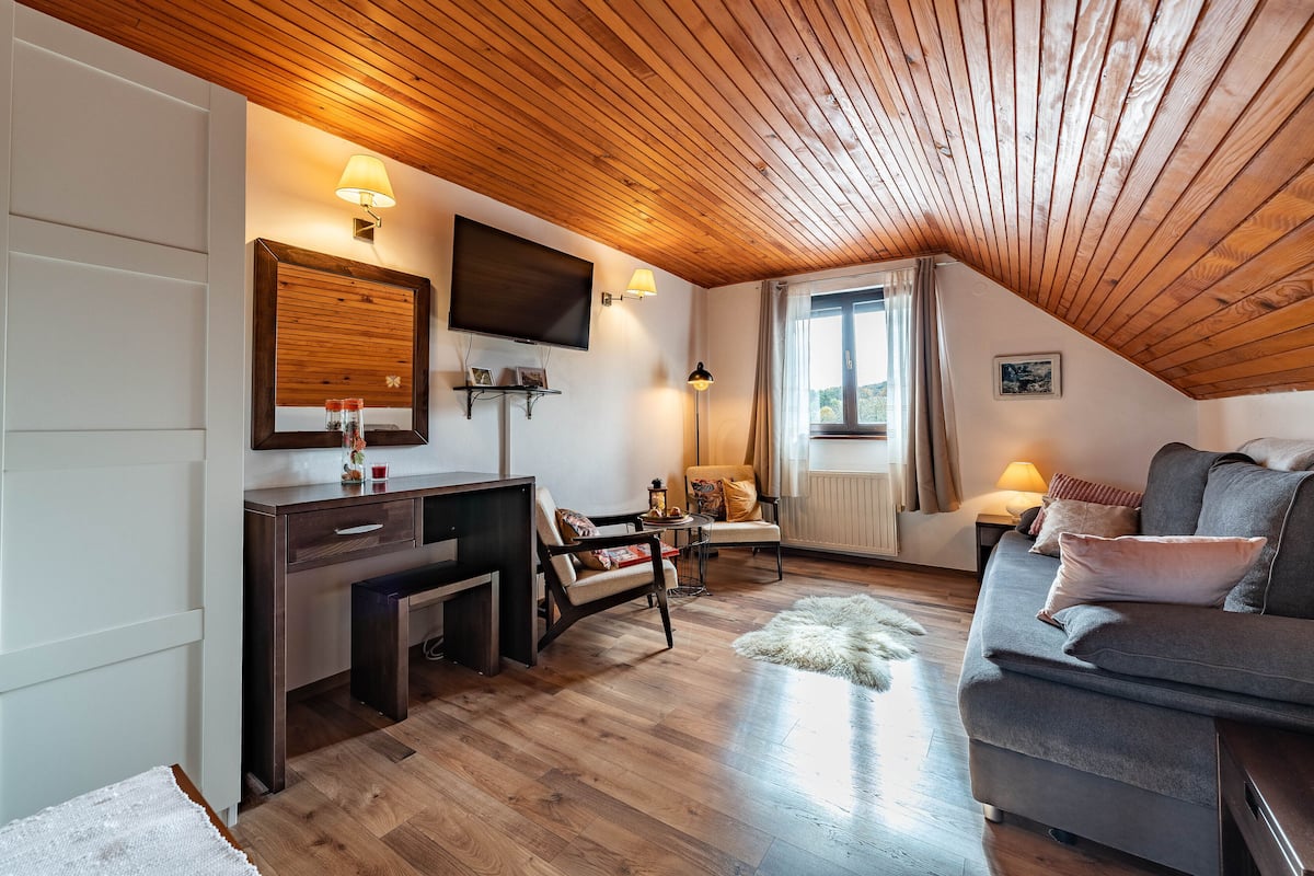 Ein gemütliches Wohnzimmer mit Holzbalkendecke, einem Flachbildfernseher, einer Couch und einem Couchtisch.