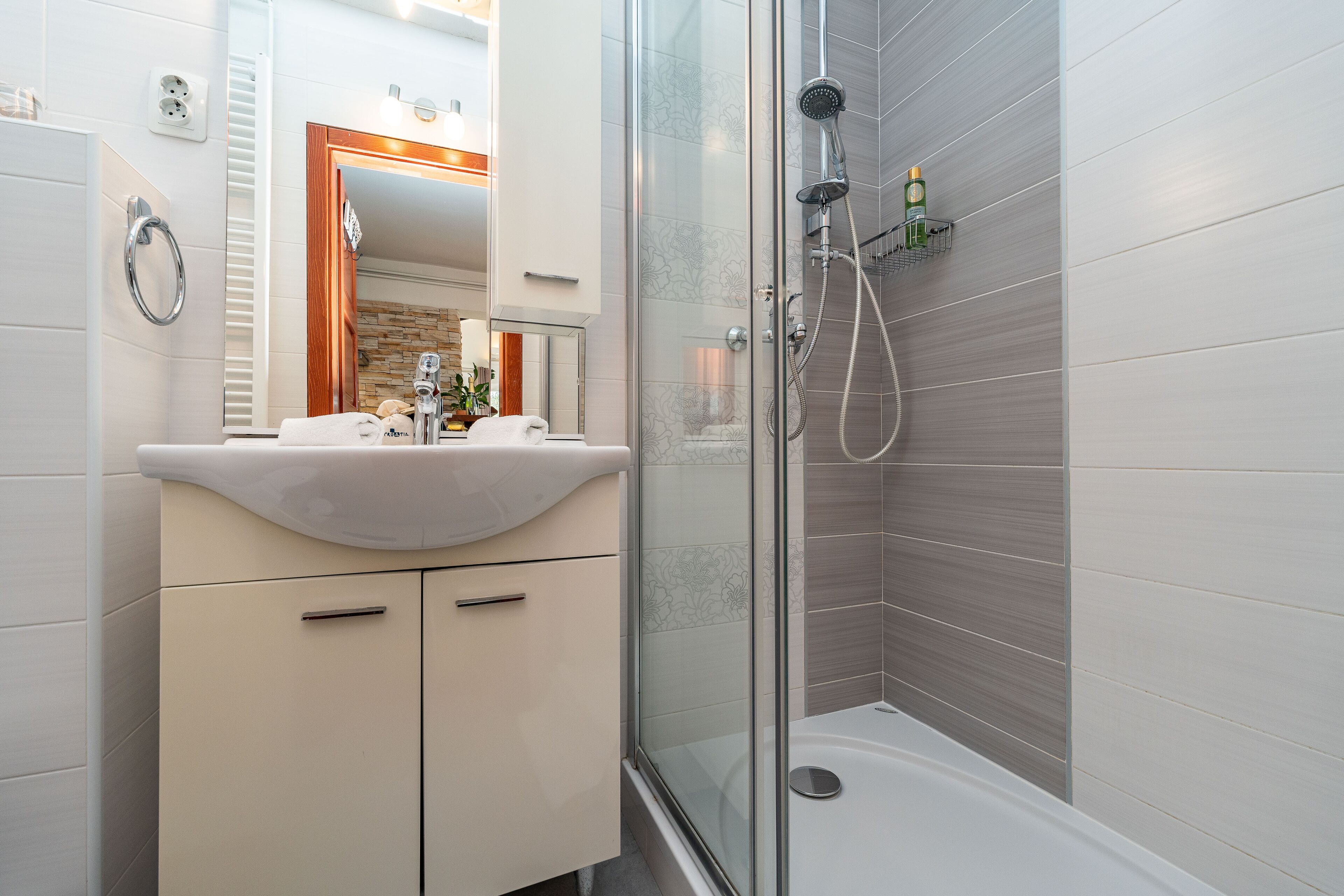Een moderne badkamer met een douche met glazen wand, een wastafel met spiegel en een handdoekrek.