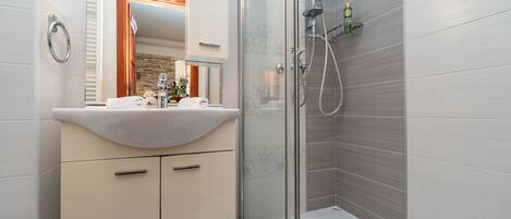 Een moderne badkamer met een douche met glazen wand, een wastafel met spiegel en een handdoekrek.