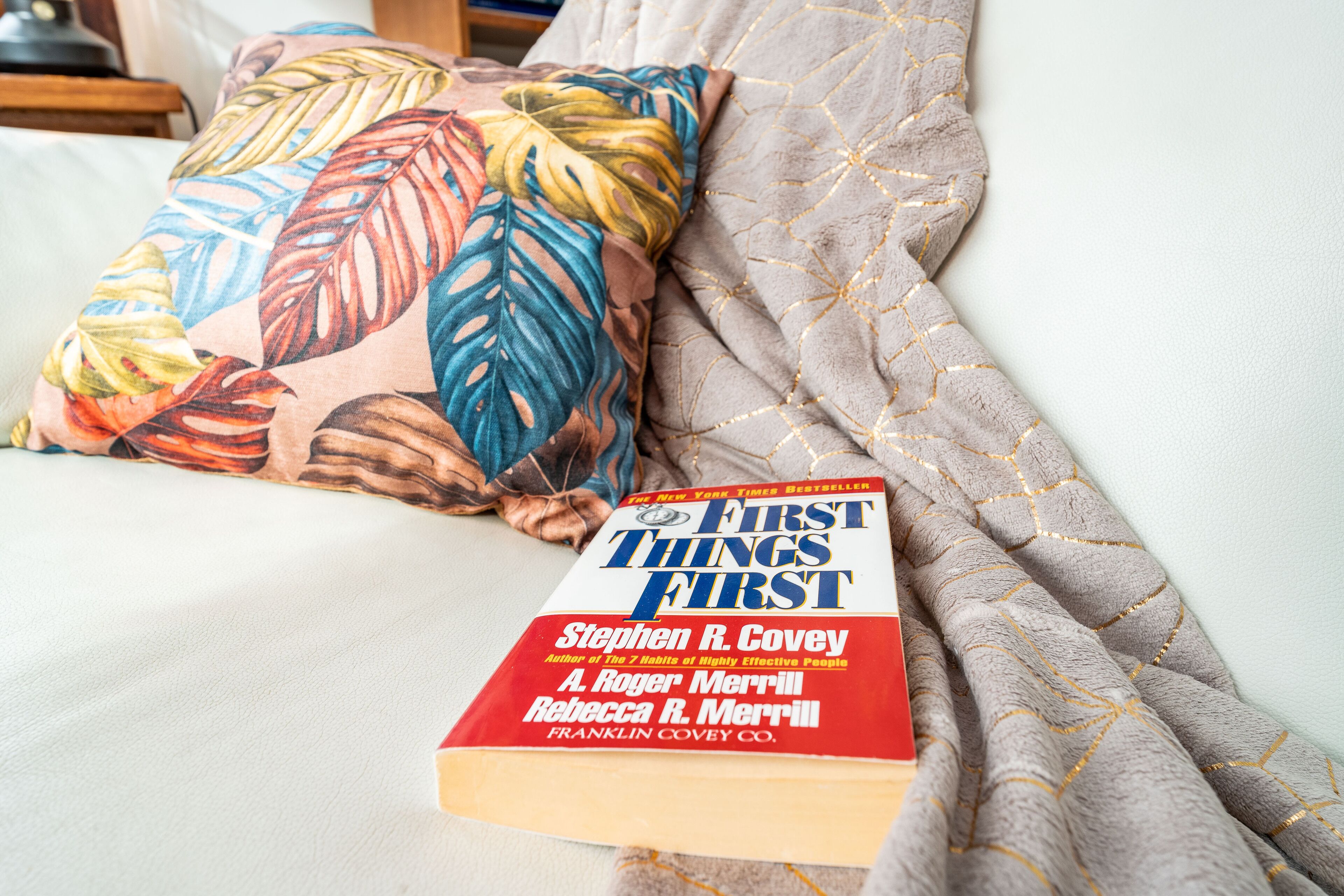 A book titled 'First Things First' by Stephen R. Covey on a bed with a patterned pillow and a textured blanket.