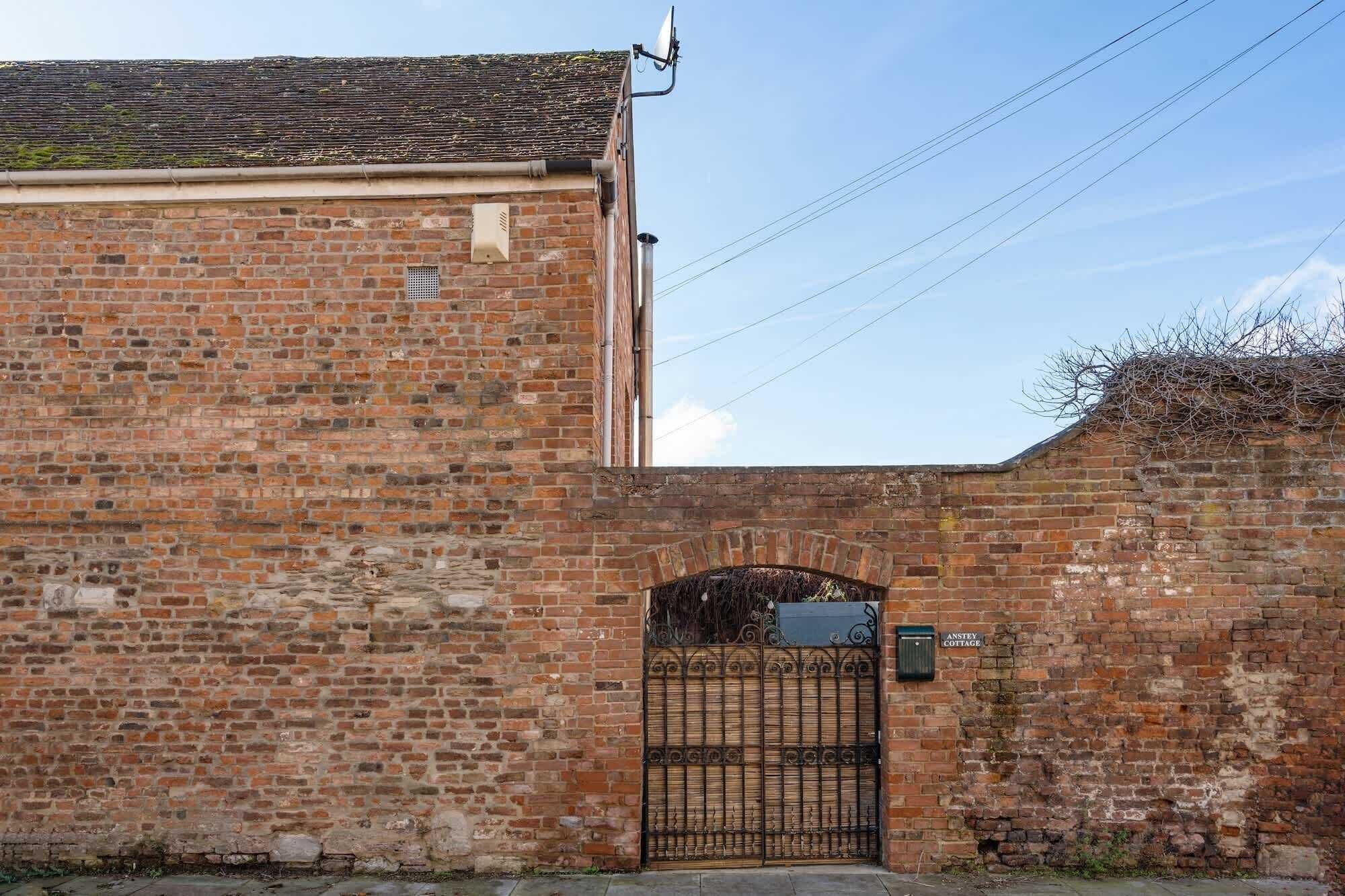 A brick building with a metal gate and a sign reading "Anstey Cottage."
