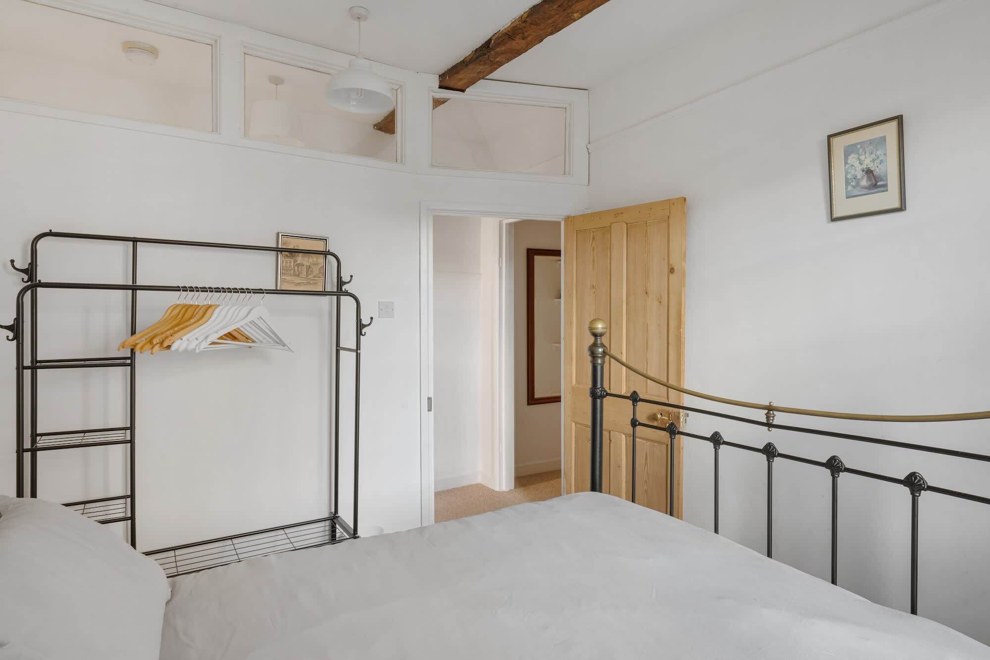 Un dormitorio con estructura de cama metálica, colchón blanco, armario metálico con ropa y puerta de madera que da a otra habitación.