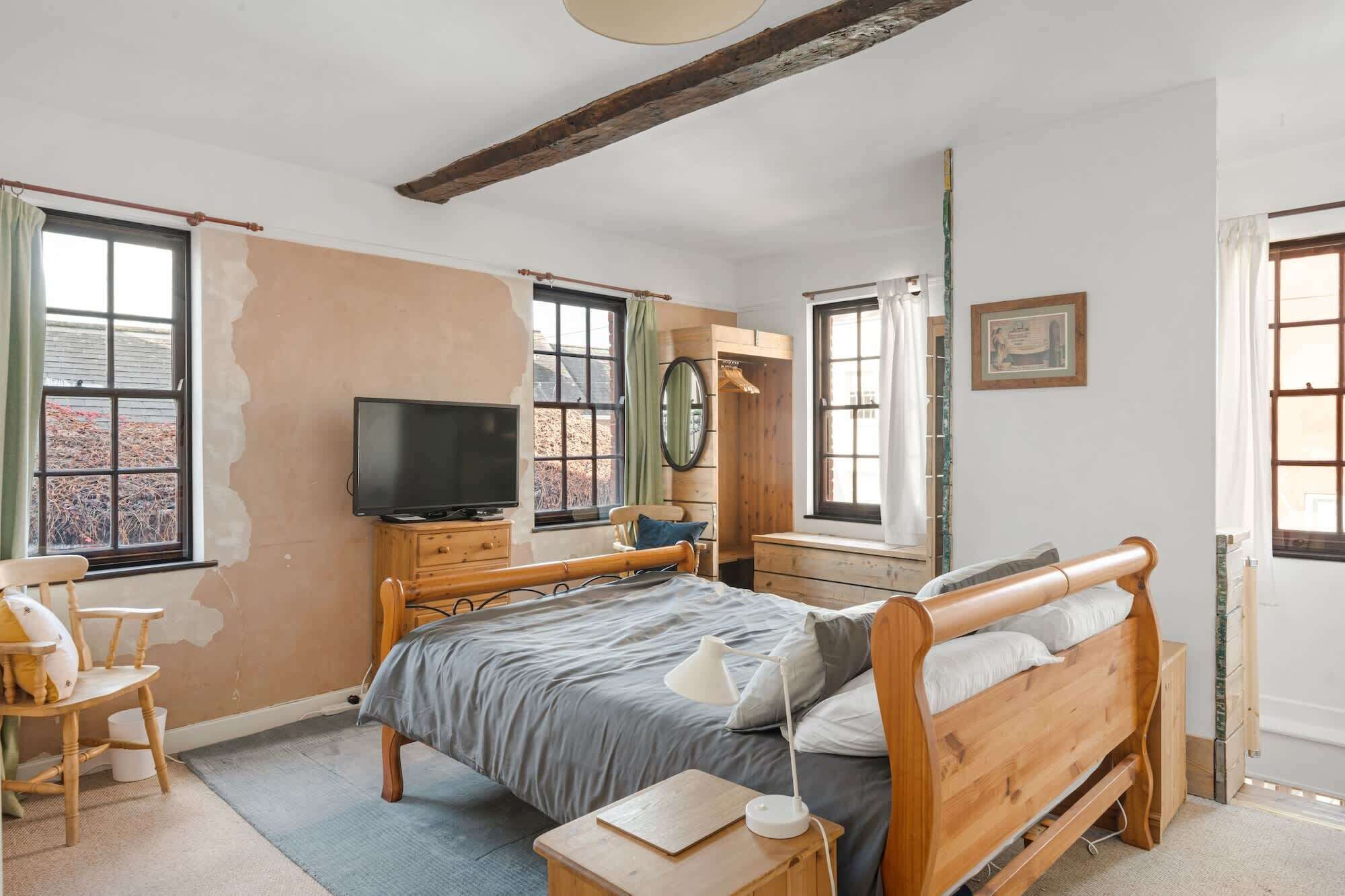 A bedroom with a wooden bed, a TV on a wooden dresser, and a window with a view of a building.