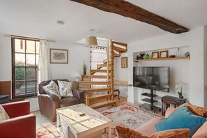 Una sala de estar con una escalera espiral de madera, un sofá, una mesa de centro y un televisor.