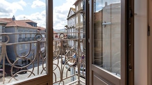 Uitzicht vanuit een raam met sierlijk metalen hekwerk, over een straat met historische gebouwen en kinderaardewerktegels.