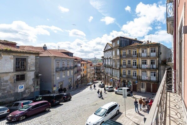A cobblestone street with historic buildings, a white car, and pedestrians.