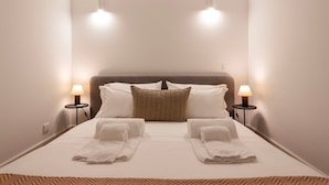 Een keurig opgemaakt bed met twee kussens, twee nachtlampjes en twee opgevouwen handdoeken op het bed.