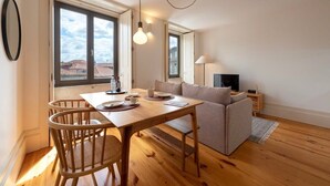 Una sala de estar moderna con una mesa de comedor de madera, dos sillas, un sofá y una televisión.