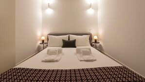 Una habitación de hotel con una cama bien hecha, dos lámparas de noche y una colcha estampada.