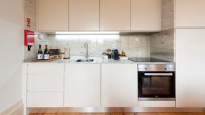Una cocina moderna con armarios blancos, un lavamanos de acero inoxidable, un horno empotrado y un salpicadero de mármol.