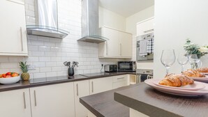 A modern kitchen with white cabinets, a stainless steel range hood, a microwave, and a toaster. There are two wine glasses and a plate with croissants on the counter. - Bloomfield 7 (Lancaster)