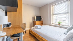 A modern bedroom with a wooden bed, a desk with a chair, a television on a wooden stand, and a window with blinds. - Bloomfield 7 (Lancaster)