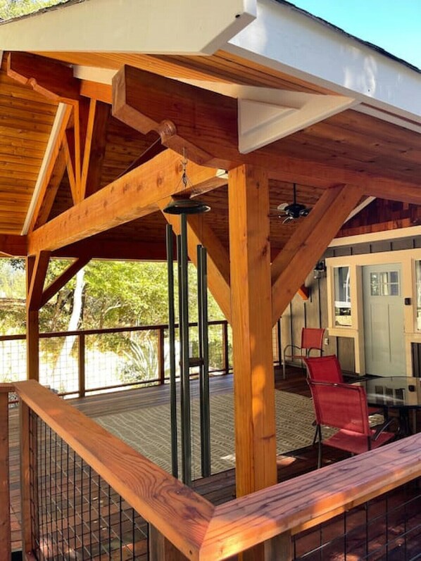 Una terraza de madera con barandilla, un comedor con sillas y vistas al exterior.