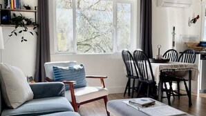 Una sala de estar moderna con un sofá, una mesa de comedor con sillas, una ventana con cortinas y una estantería.