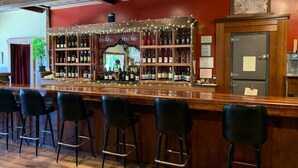 Zona de bar amb un taulell de fusta, tamborets negres i estanteries plenes de garrafes.