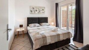 A bedroom with a bed, a small bedside table, a wall-mounted light, a window with curtains, and a door. - Apartment Tino by Interhome (Zadar/Sukošan)