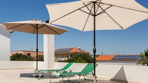 A rooftop terrace with two green lounge chairs and two large umbrellas, a clear blue sky, and buildings with solar panels in the background. - Apartment Tino by Interhome (Zadar/Sukošan)