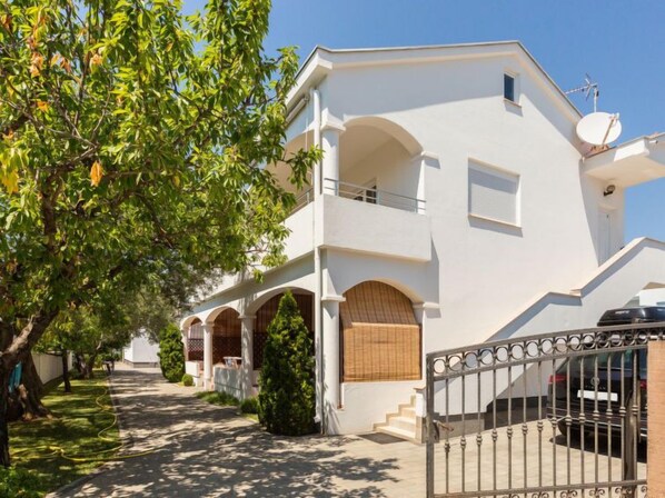 A two-story white building with a balcony, a satellite dish, and a gated driveway.