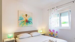 Une chambre d’hôtel avec un lit, deux tables de chevet, une lampe de chevet, une fenêtre avec des rideaux et un tableau au mur.