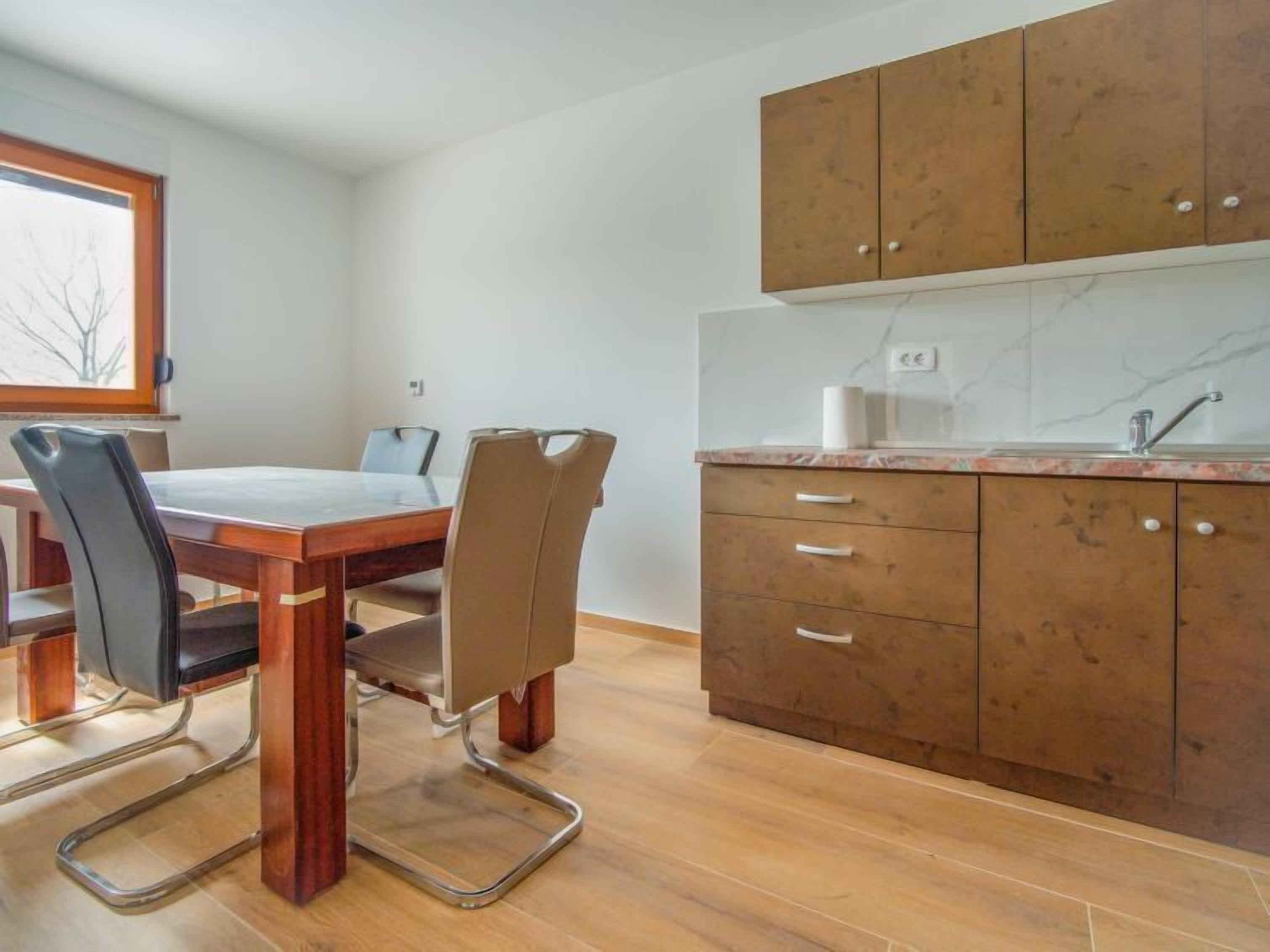 A modern kitchen with wooden cabinets, a marble countertop, and a dining area with a table and chairs.