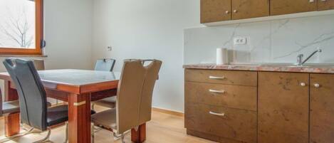 A modern kitchen with wooden cabinets, a marble countertop, and a dining area with a table and chairs.