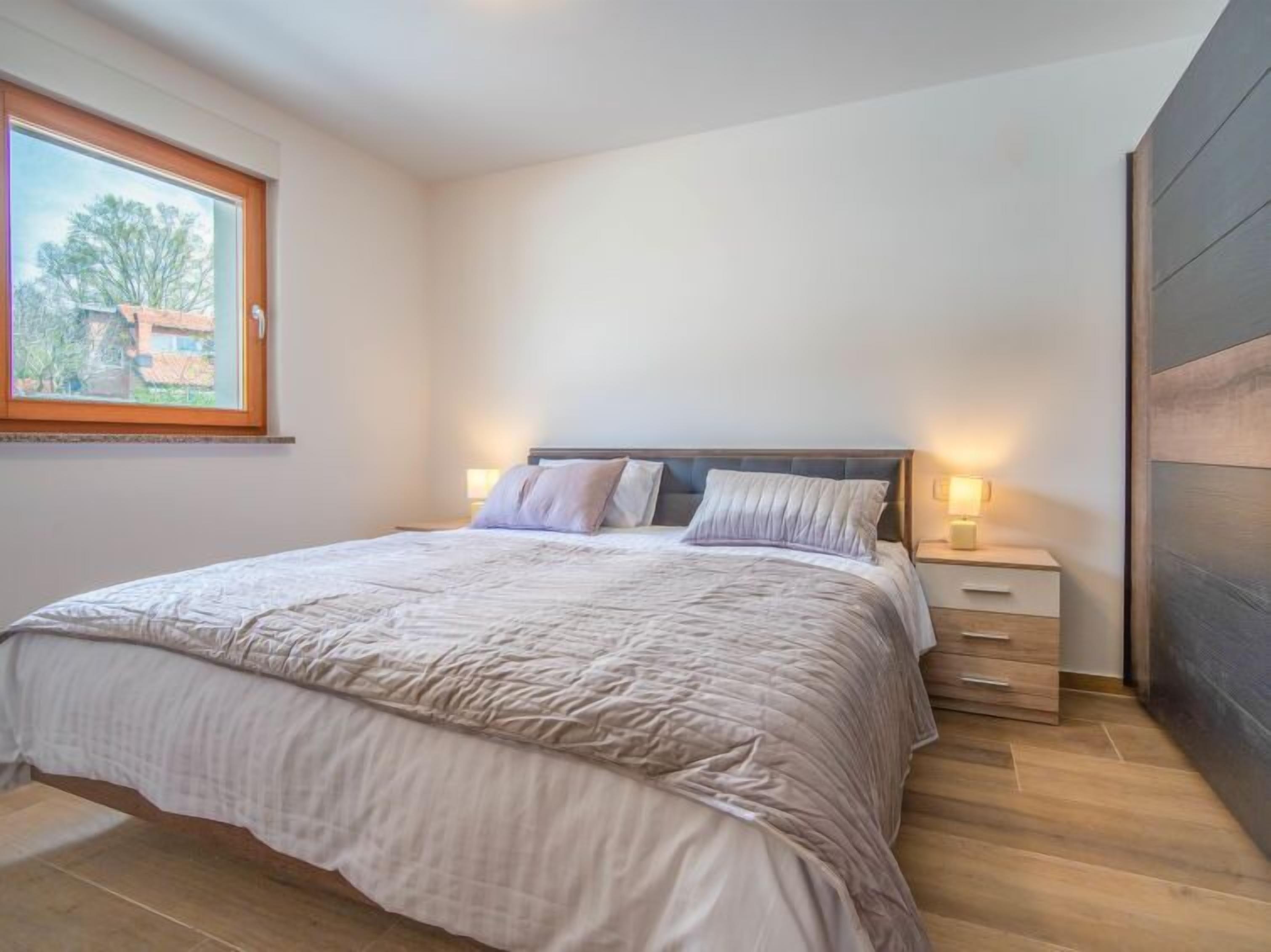 A bedroom with a bed, bedside tables, and a window.