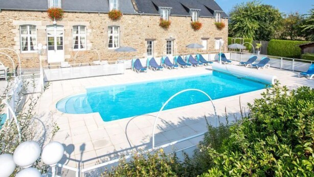 Un bâtiment en pierre doté d’une piscine, de chaises longues et surplombant un ciel d’un bleu limpide.