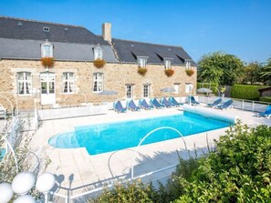 A stone building with a swimming pool, lounge chairs, and a clear blue sky.