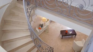 Un escalier en colimaçon avec une rampe en métal, une petite table avec une lampe et une chaise dans une pièce dont le sol est recouvert d’une moquette beige.