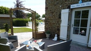 Un espace extérieur aménagé avec des chaises en osier et une table en verre, un bâtiment en pierre avec une enseigne indiquant la présence d’un spa, et une porte blanche.