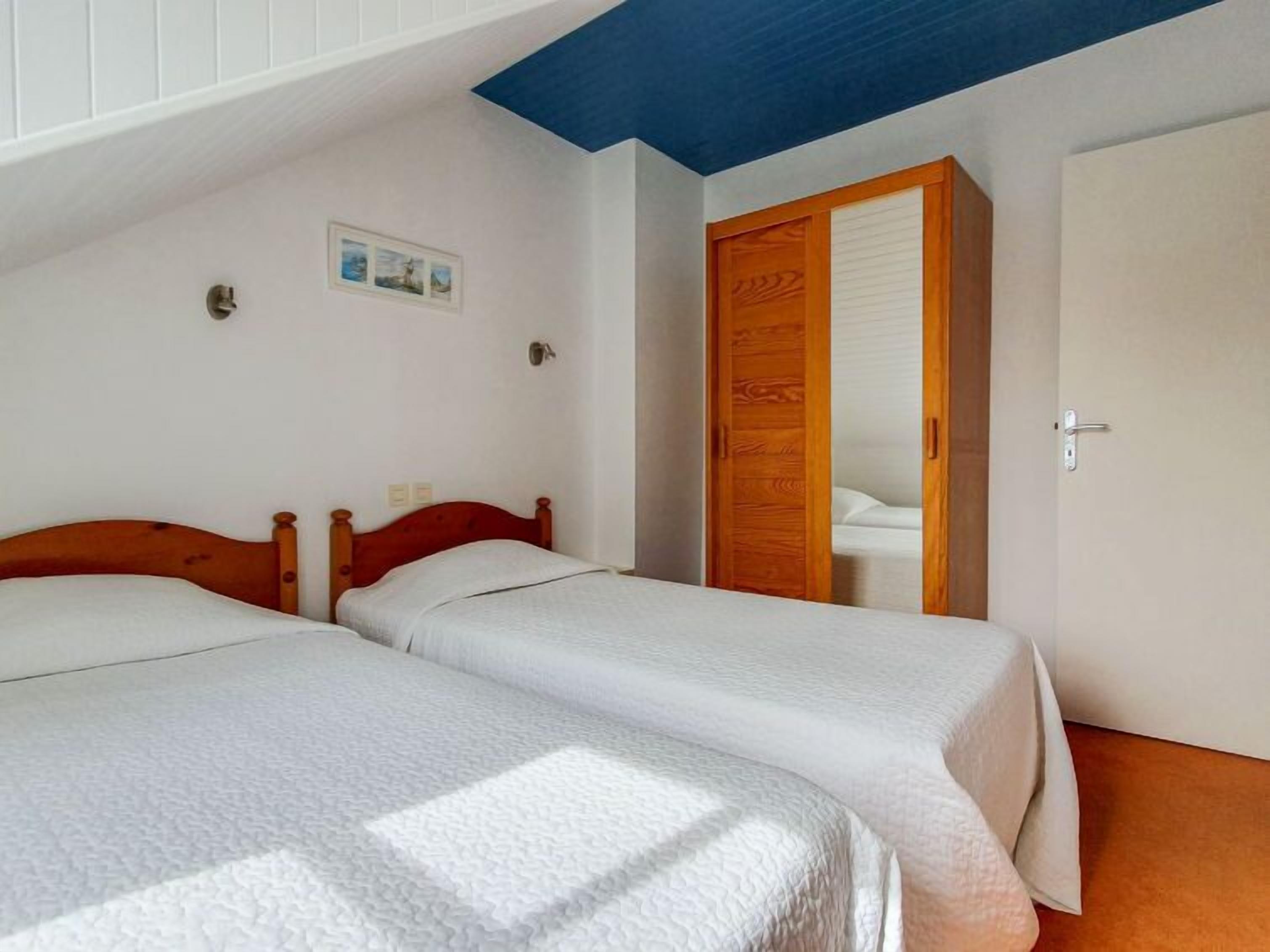 Een slaapkamer met twee bedden, een houten garderobe en een witte deur.