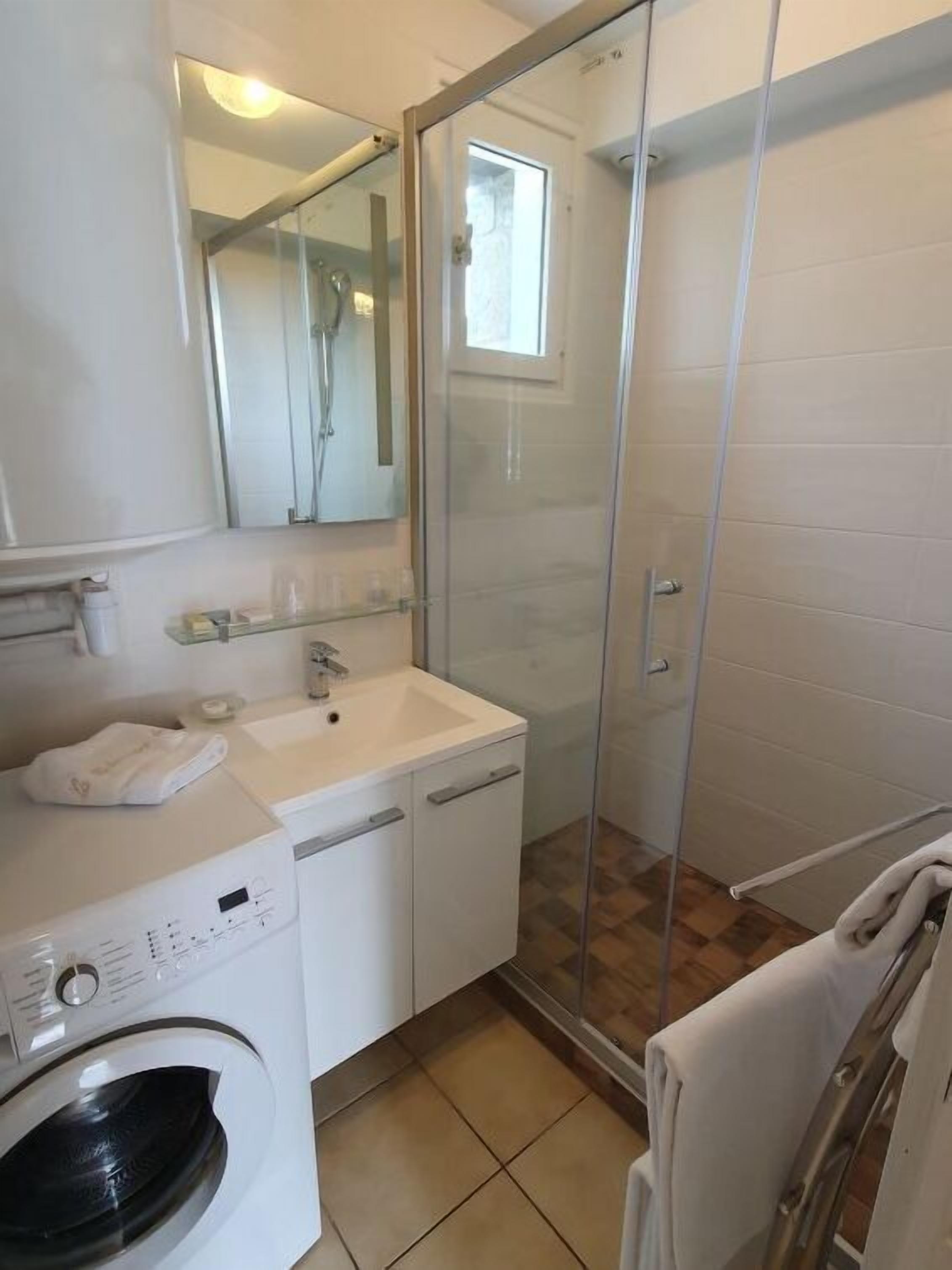 Een badkamer met een wasmachine, een wastafel, een glazen douchecabine en een handdoekhouder.