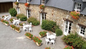 Un edificio de piedra con varias ventanas y un patio con mesas y sillas blancas.