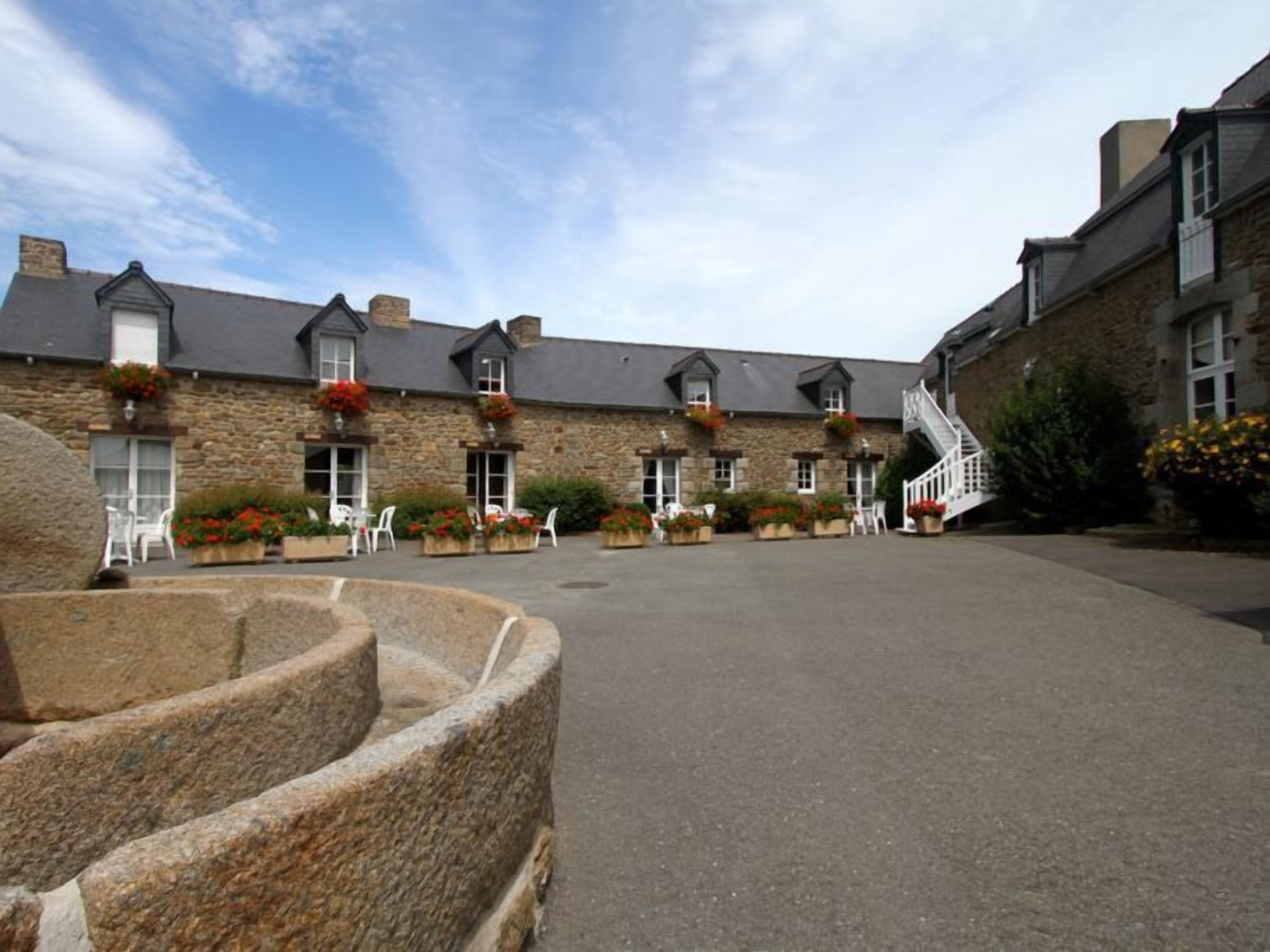 A stone building with multiple windows, a staircase, and outdoor seating with potted plants.