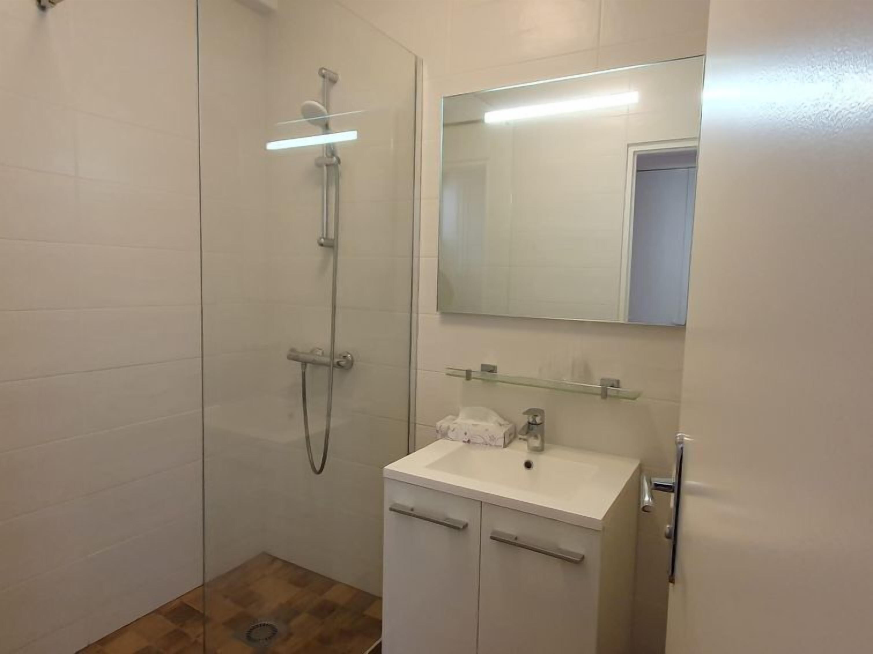 A modern bathroom with a glass-enclosed shower, a white sink with a mirror above it, and a small cabinet below.