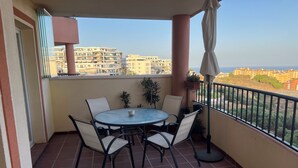 Un balcone con un tavolo rotondo e sedie, piante in vaso e vista su edifici sullo sfondo.