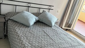 Un letto rifatto con cura, coperta a motivi geometrici e due cuscini, un comodino e una finestra con vista sull'esterno.