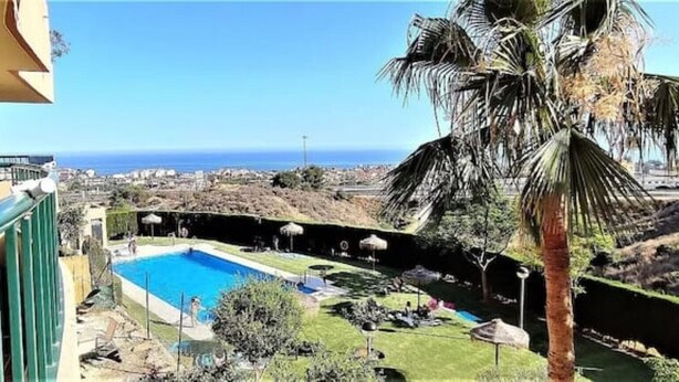 Area piscina con vista sull'oceano, circondata da palme e un paesaggio collinare.