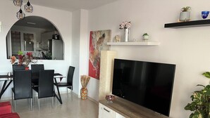 Un soggiorno moderno con una TV a schermo piatto, un'area pranzo con sedie e tavolo, e una cucina visibile tramite un arco.
