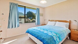 A bedroom with a bed, a nightstand, a lamp, a window with curtains, and a ceiling light.